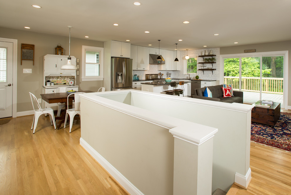 Mid-sized transitional l-shaped open plan kitchen in DC Metro with a farmhouse sink, white cabinets, granite benchtops, white splashback, subway tile splashback, stainless steel appliances, light hardwood floors, with island and shaker cabinets.