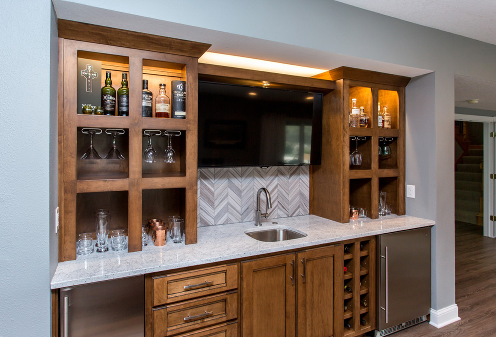 This is an example of a mid-sized transitional galley seated home bar in Other with an undermount sink, recessed-panel cabinets, medium wood cabinets, quartz benchtops, grey splashback, ceramic splashback, vinyl floors and beige floor.