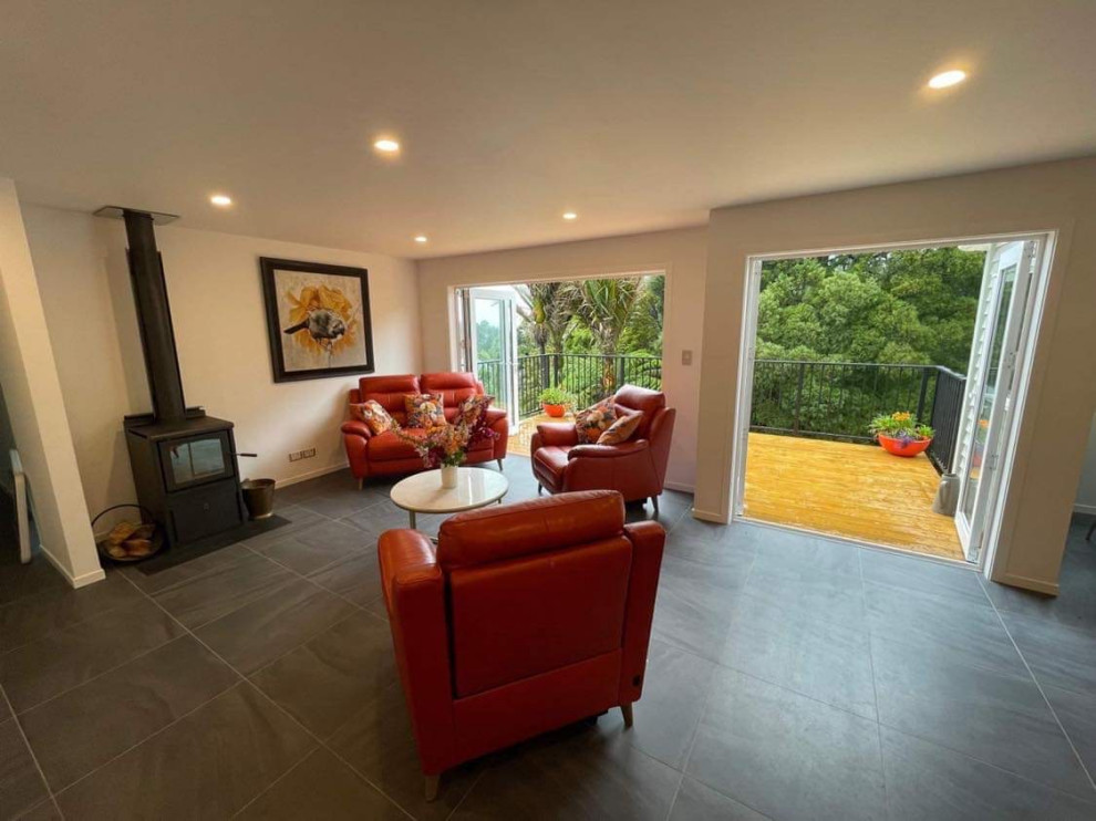 На фото: открытая гостиная комната среднего размера в стиле модернизм с белыми стенами, полом из керамической плитки, печью-буржуйкой, фасадом камина из штукатурки и серым полом с