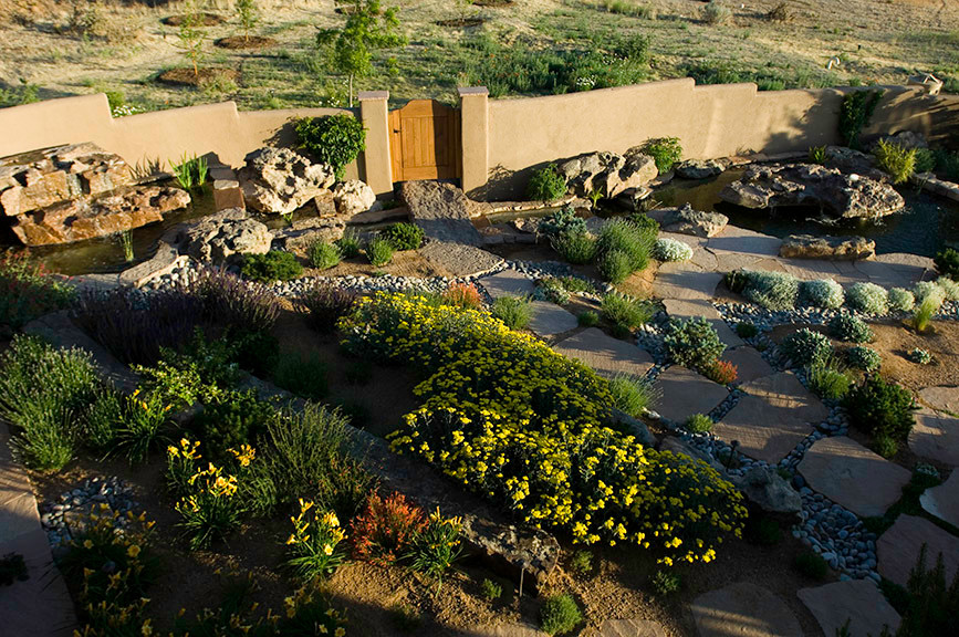 Photo of a large partial sun backyard gravel water fountain landscape.