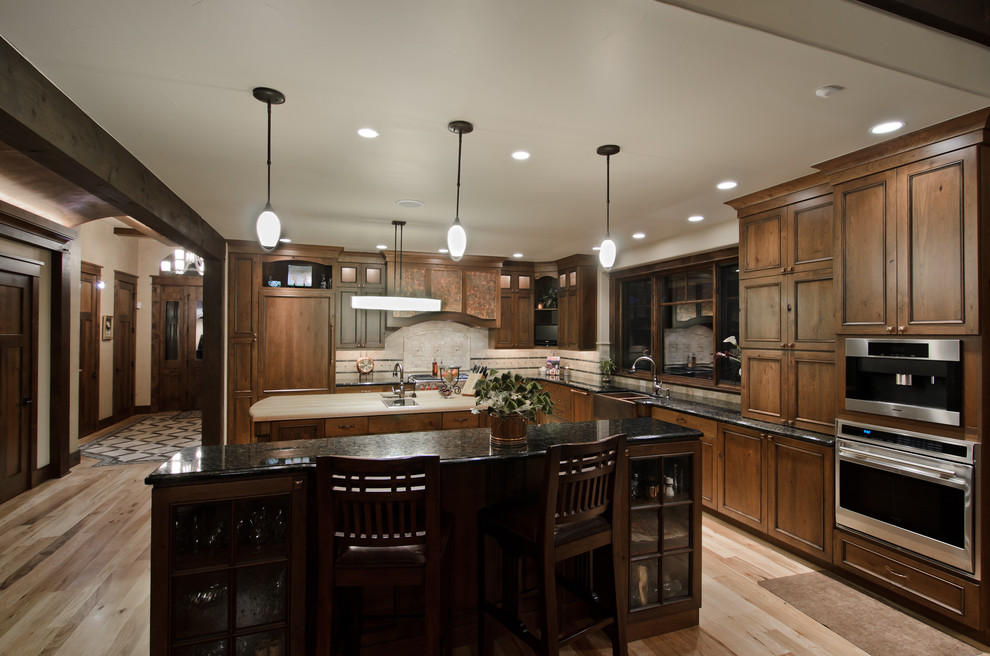 Photo of a traditional l-shaped kitchen in Denver with a farmhouse sink, recessed-panel cabinets, dark wood cabinets, beige splashback and stainless steel appliances.