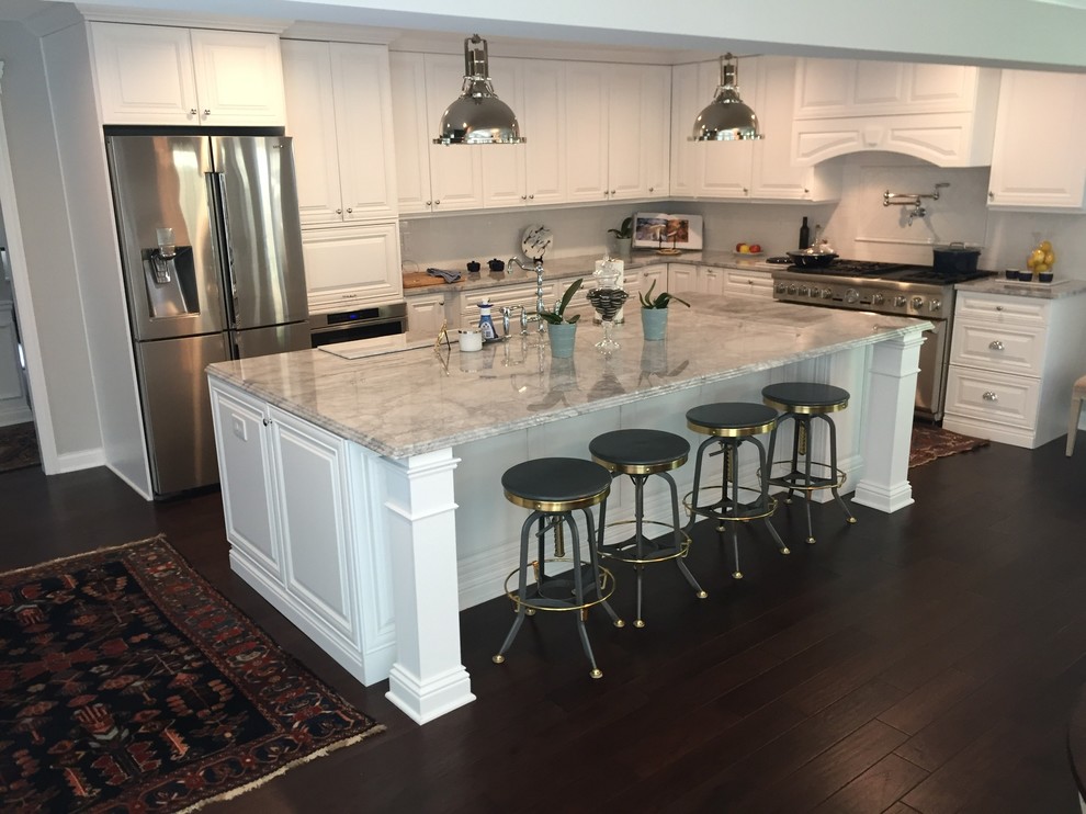 This is an example of a large transitional galley kitchen in Cleveland with a farmhouse sink, raised-panel cabinets, white cabinets, marble benchtops, white splashback, ceramic splashback, stainless steel appliances, dark hardwood floors, with island and brown floor.