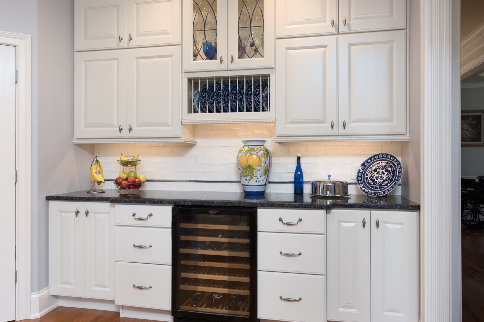 Large transitional single-wall light wood floor and brown floor open concept kitchen photo with a farmhouse sink, raised-panel cabinets, white cabinets, quartz countertops, white backsplash, ceramic backsplash, stainless steel appliances, an island and white countertops