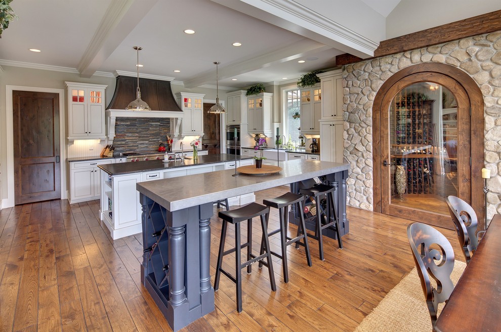 Design ideas for a country l-shaped eat-in kitchen in Minneapolis with a farmhouse sink, shaker cabinets, white cabinets, grey splashback, stone tile splashback, white appliances, dark hardwood floors and multiple islands.