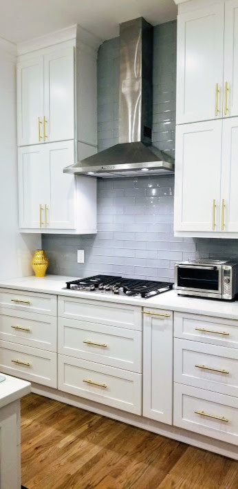 Example of a large transitional l-shaped medium tone wood floor and brown floor open concept kitchen design in Miami with an undermount sink, shaker cabinets, white cabinets, glass tile backsplash, stainless steel appliances, an island, white countertops, quartz countertops and gray backsplash