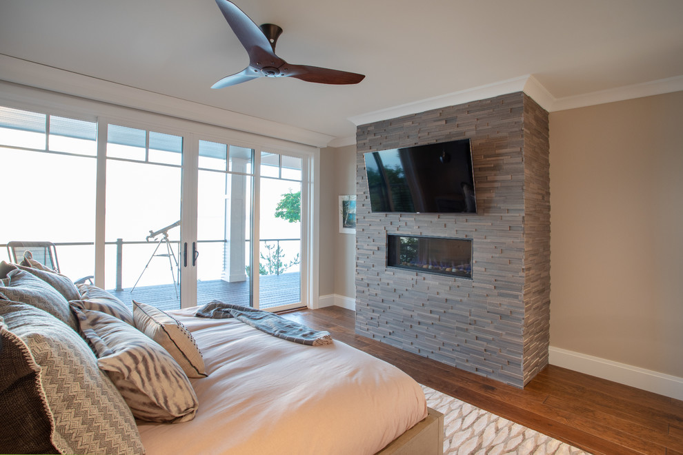 Photo of a large contemporary master bedroom in Other with beige walls, medium hardwood floors, a standard fireplace, a stone fireplace surround and brown floor.