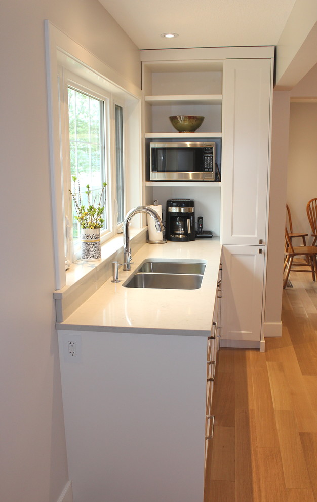 Inspiration for a large transitional l-shaped light wood floor home design remodel with an undermount sink, shaker cabinets, white cabinets, quartz countertops, white backsplash, ceramic backsplash, stainless steel appliances and an island