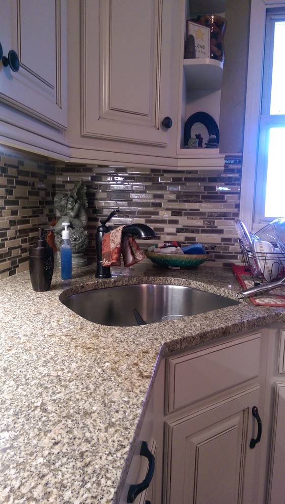 Inspiration for a mid-sized transitional l-shaped laminate floor eat-in kitchen remodel with an undermount sink, raised-panel cabinets, white cabinets, granite countertops, multicolored backsplash, mosaic tile backsplash, white appliances and no island