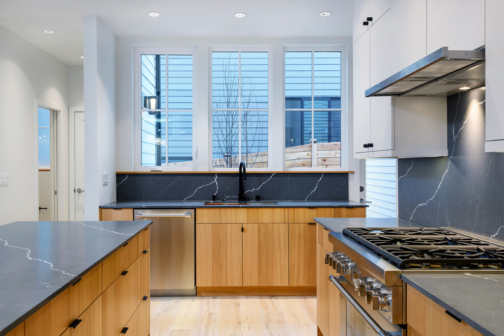 This is an example of a mid-sized contemporary u-shaped eat-in kitchen in Seattle with an undermount sink, flat-panel cabinets, light wood cabinets, quartz benchtops, grey splashback, engineered quartz splashback, stainless steel appliances, light hardwood floors, with island and grey benchtop.