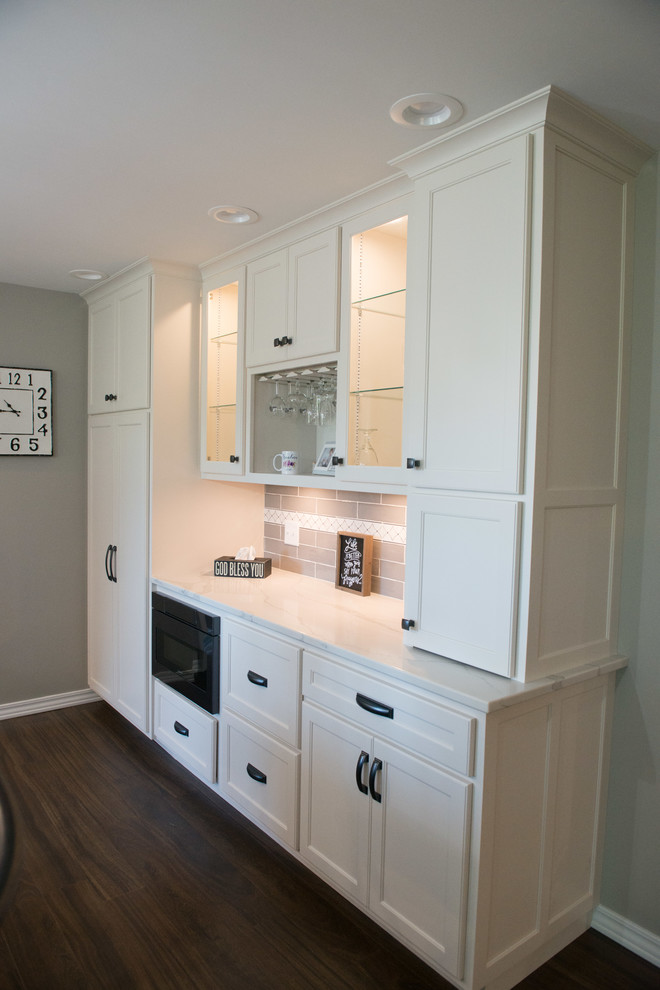 Large transitional u-shaped laminate floor and brown floor eat-in kitchen photo with a double-bowl sink, shaker cabinets, white cabinets, quartz countertops, gray backsplash, subway tile backsplash, stainless steel appliances, an island and white countertops