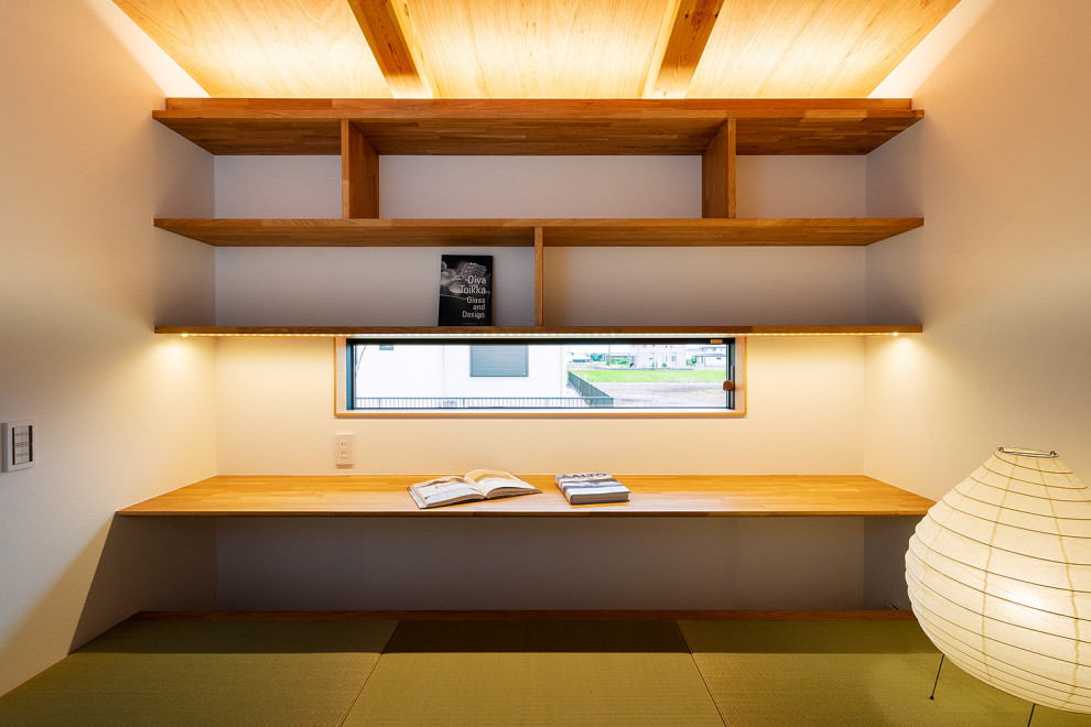 Inredning av ett litet avskilt allrum, med ett bibliotek, vita väggar, tatamigolv, en öppen vedspis, en spiselkrans i trä och grönt golv