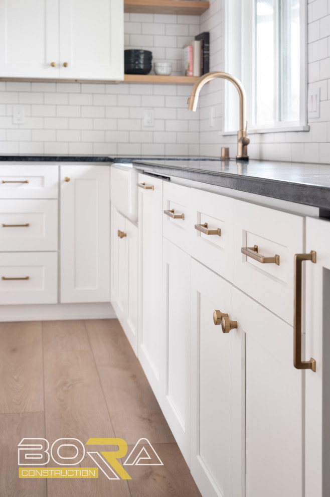 Mid-sized transitional u-shaped medium tone wood floor and brown floor eat-in kitchen photo in Seattle with shaker cabinets, white cabinets, quartz countertops, white backsplash, ceramic backsplash, stainless steel appliances, an island and black countertops