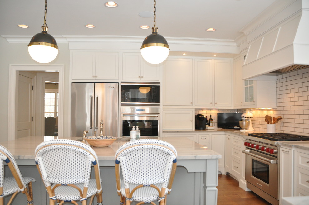 Large transitional l-shaped medium tone wood floor and brown floor open concept kitchen photo in Cleveland with an undermount sink, recessed-panel cabinets, white cabinets, marble countertops, white backsplash, subway tile backsplash, stainless steel appliances, an island and white countertops