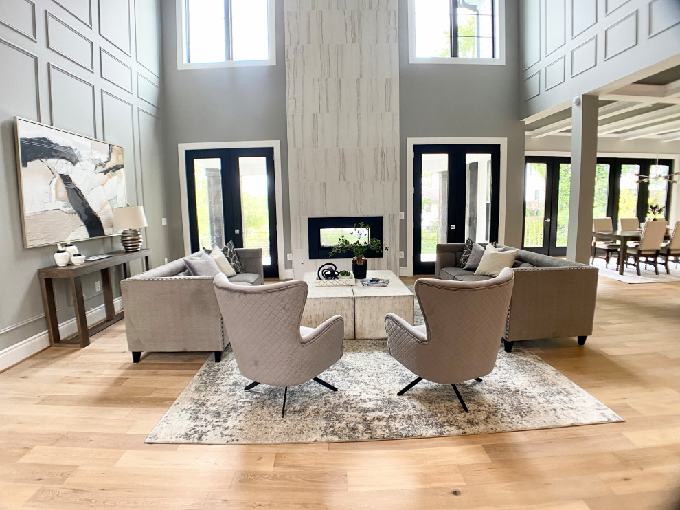 Expansive rural open plan living room in DC Metro with grey walls, light hardwood flooring, a two-sided fireplace, a tiled fireplace surround, beige floors, a coffered ceiling and panelled walls.