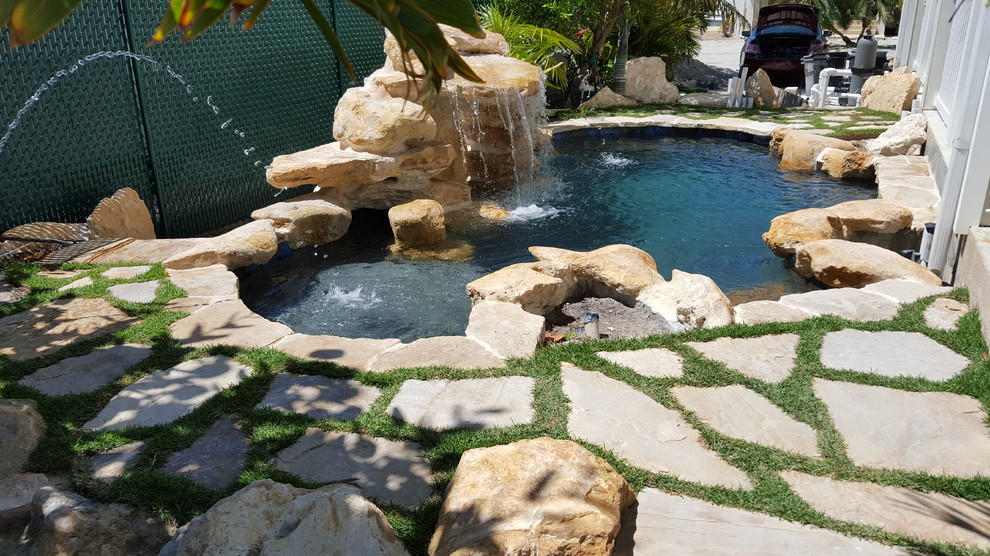 This is an example of a small tropical backyard custom-shaped natural pool in Miami with a water feature and natural stone pavers.