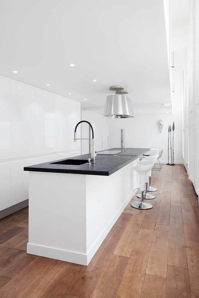 Photo of a mid-sized contemporary galley eat-in kitchen in Paris with an undermount sink, flat-panel cabinets, white cabinets, panelled appliances, medium hardwood floors and with island.