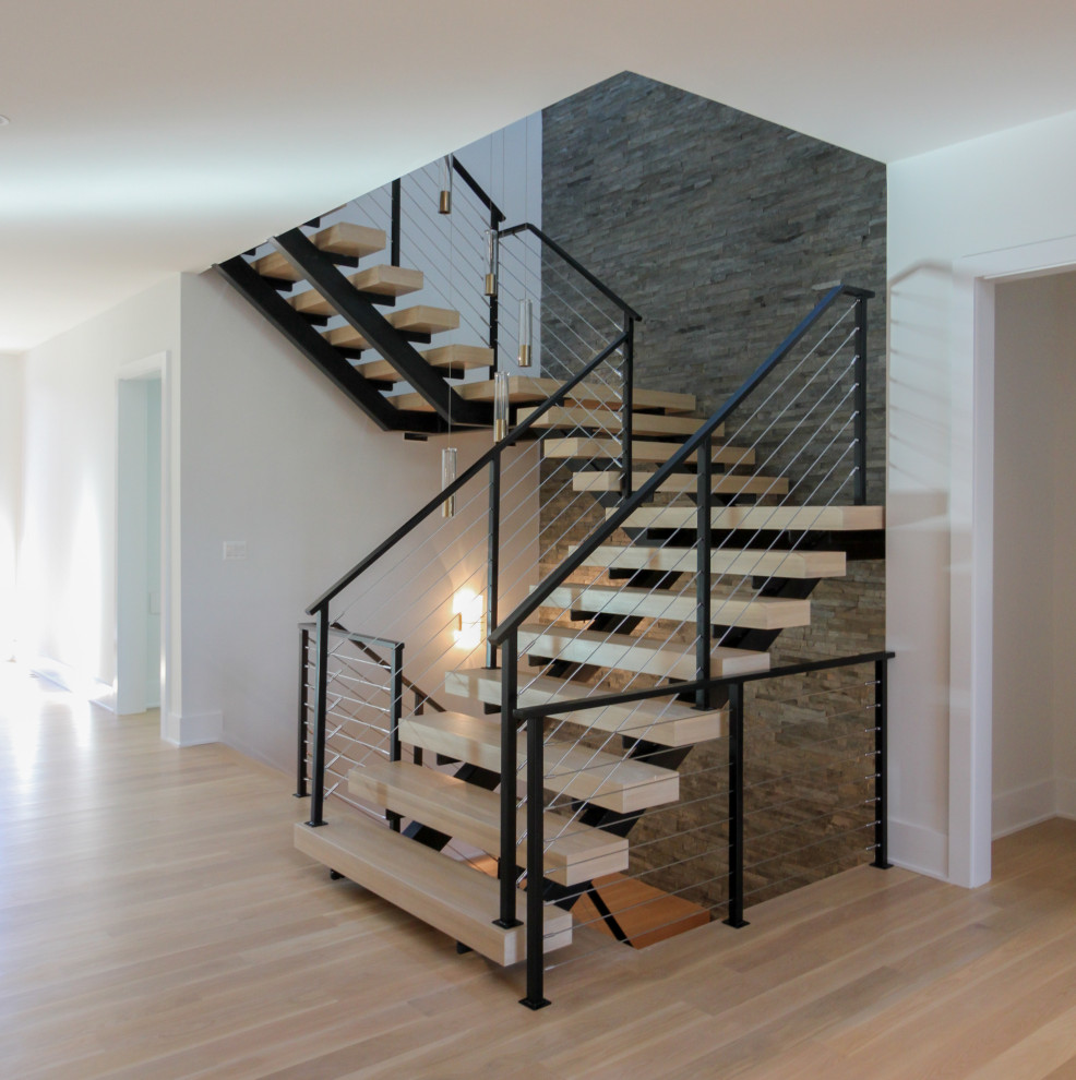 Идея дизайна: большая лестница на больцах в стиле фьюжн с деревянными ступенями, металлическими перилами и кирпичными стенами