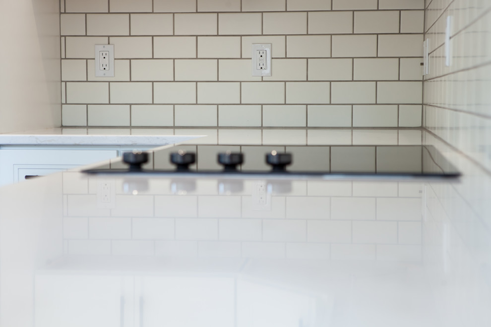 Large transitional l-shaped dark wood floor and brown floor home design photo with an undermount sink, recessed-panel cabinets, white cabinets, quartz countertops, white backsplash, subway tile backsplash, stainless steel appliances and an island
