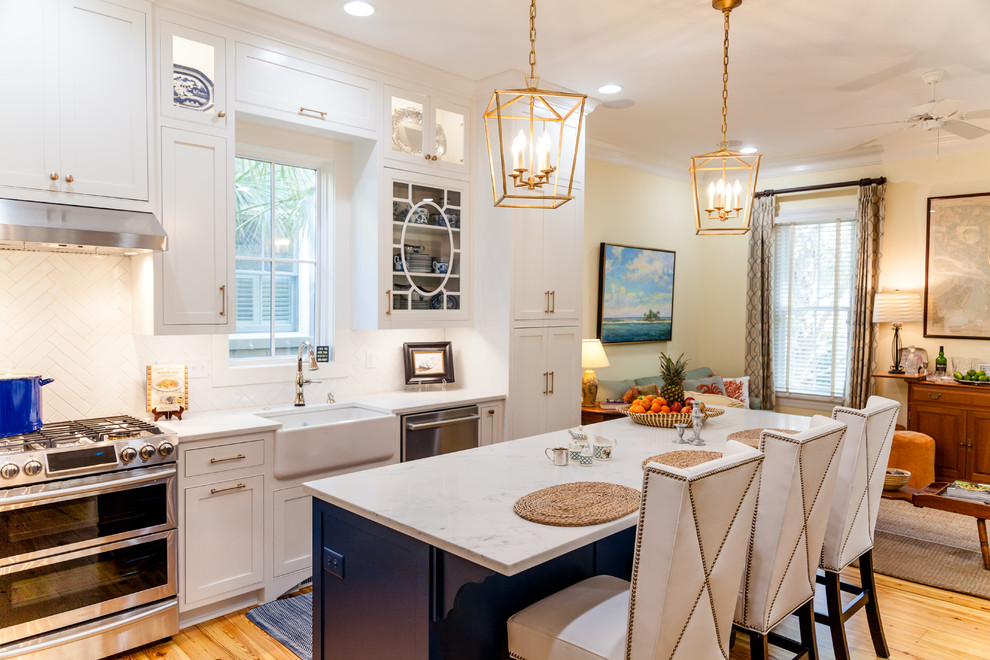 Photo of a large transitional l-shaped open plan kitchen in Charleston with a farmhouse sink, white cabinets, quartz benchtops, white splashback, stainless steel appliances, medium hardwood floors, with island and recessed-panel cabinets.