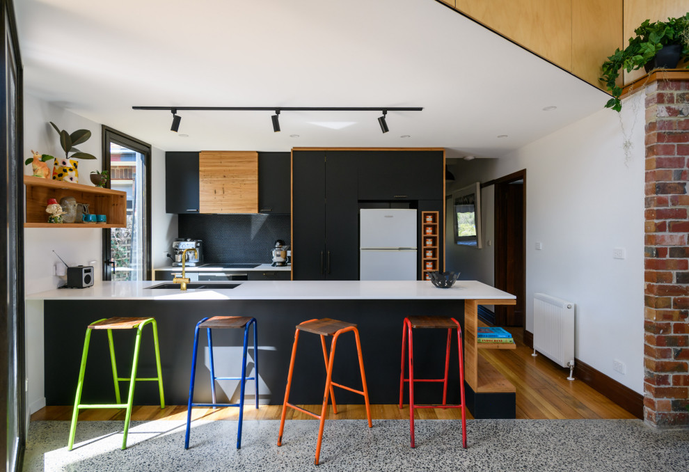 Design ideas for a contemporary galley open plan kitchen in Melbourne with a double-bowl sink, flat-panel cabinets, black cabinets, black splashback, white appliances, medium hardwood floors, a peninsula, brown floor and white benchtop.