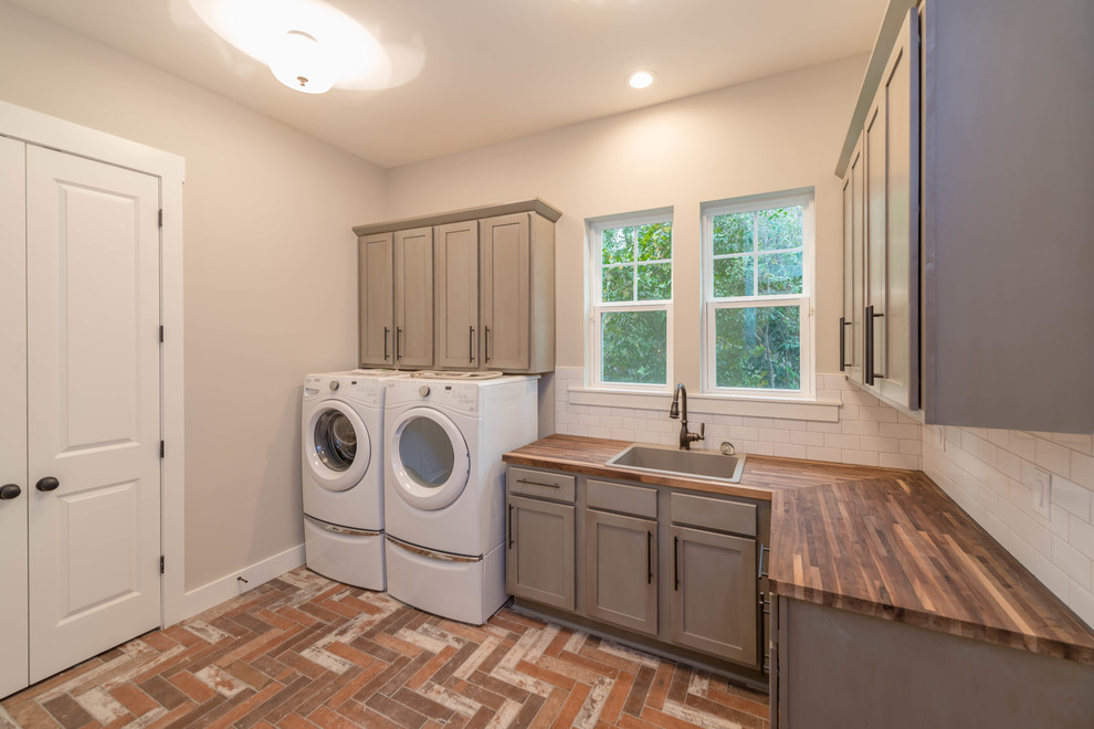 Mid-sized beach style l-shaped laundry room in Jacksonville with a drop-in sink, grey cabinets, wood benchtops, grey walls, ceramic floors, a side-by-side washer and dryer, brown benchtop and shaker cabinets.