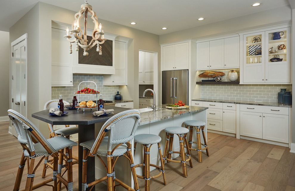 This is an example of a beach style u-shaped kitchen in Chicago with shaker cabinets, white cabinets, grey splashback, subway tile splashback, stainless steel appliances, medium hardwood floors and with island.