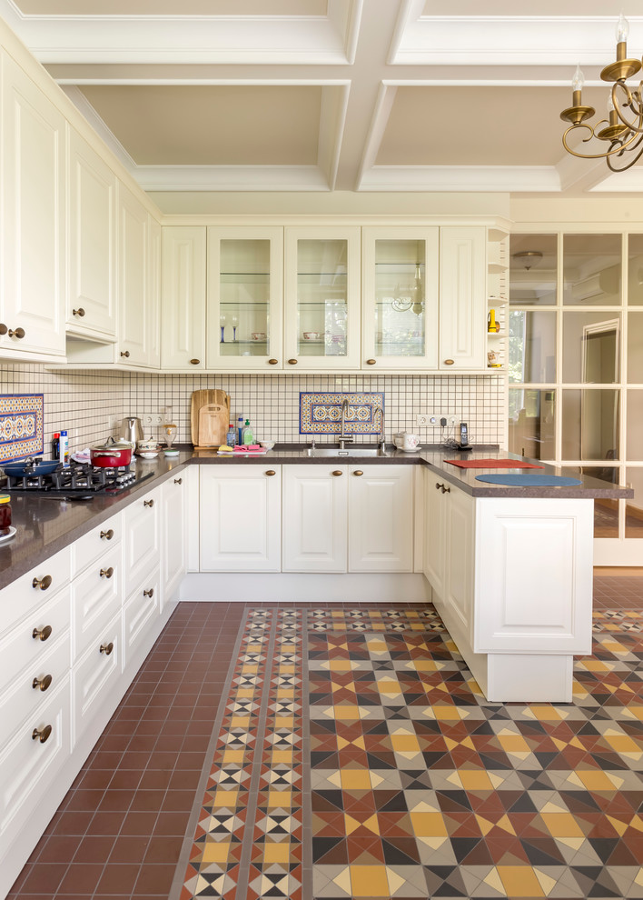 На фото: п-образная кухня с фасадами с выступающей филенкой, белыми фасадами, разноцветным фартуком, фартуком из плитки мозаики, полом из керамической плитки и полуостровом
