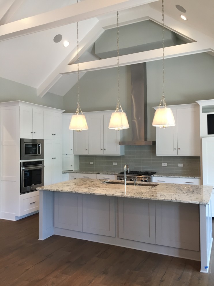 Inspiration for a mid-sized transitional l-shaped eat-in kitchen in Raleigh with a triple-bowl sink, shaker cabinets, white cabinets, granite benchtops, grey splashback, glass tile splashback, stainless steel appliances, with island, dark hardwood floors and brown floor.