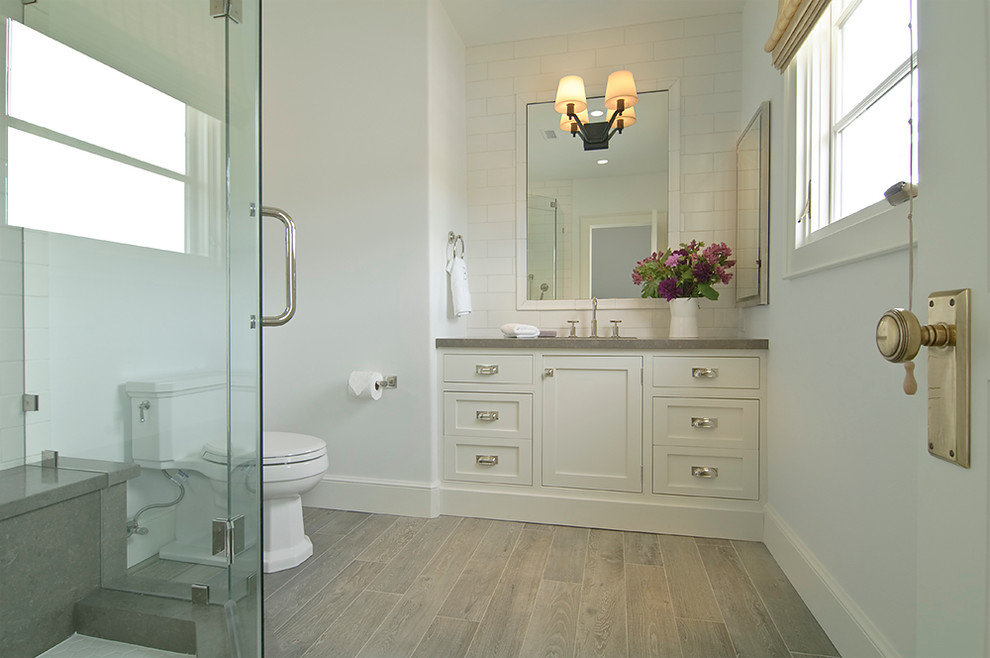 Inspiration for a small transitional 3/4 bathroom in Los Angeles with beaded inset cabinets, white cabinets, a corner shower, a one-piece toilet, white tile, subway tile, white walls, an undermount sink, limestone benchtops, porcelain floors, brown floor and grey benchtops.