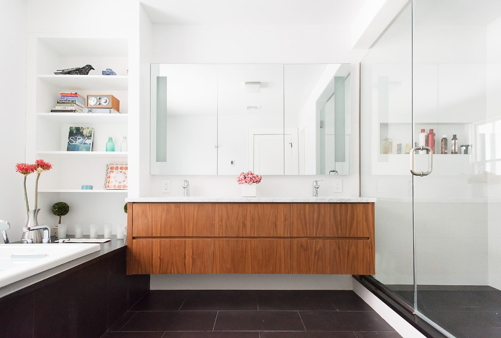 Photo of a large contemporary master bathroom in New York with flat-panel cabinets, medium wood cabinets, a drop-in tub, a corner shower, white walls, an undermount sink, marble benchtops, black floor, a hinged shower door and grey benchtops.