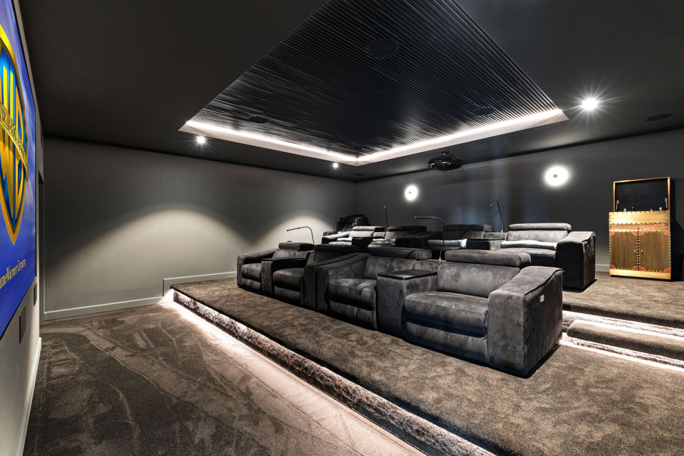 Стильный дизайн: большой изолированный домашний кинотеатр в стиле модернизм с черными стенами, ковровым покрытием, проектором и серым полом - последний тренд