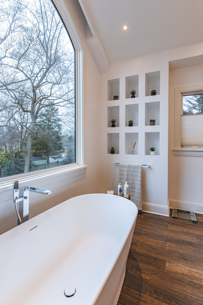 This is an example of a large modern master bathroom in DC Metro with flat-panel cabinets, beige cabinets, a freestanding tub, an alcove shower, white tile, stone tile, white walls, wood-look tile, an undermount sink, quartzite benchtops, brown floor, a hinged shower door, white benchtops, a double vanity, a floating vanity and vaulted.