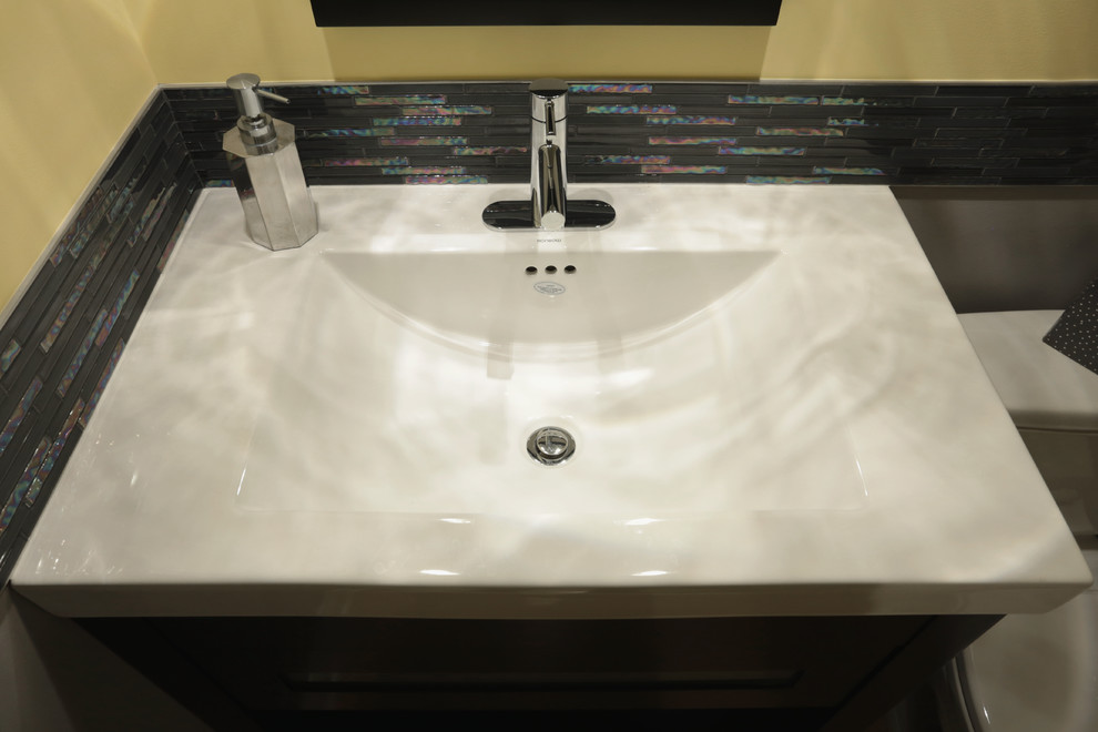 Photo of a small contemporary 3/4 bathroom in Cleveland with furniture-like cabinets, dark wood cabinets, a two-piece toilet, black tile, glass sheet wall, multi-coloured walls, light hardwood floors, an integrated sink and quartzite benchtops.