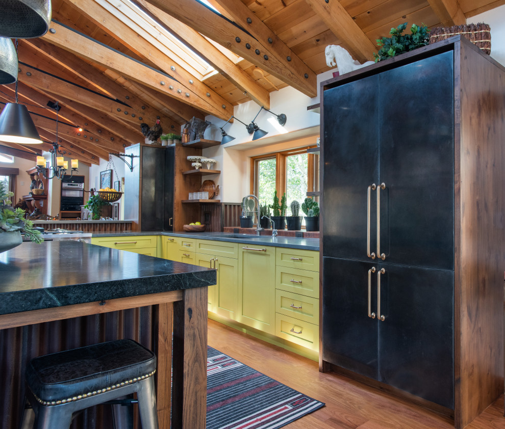 Large country l-shaped eat-in kitchen in Denver with shaker cabinets, green cabinets, soapstone benchtops, metallic splashback, medium hardwood floors, multiple islands, black benchtop and exposed beam.