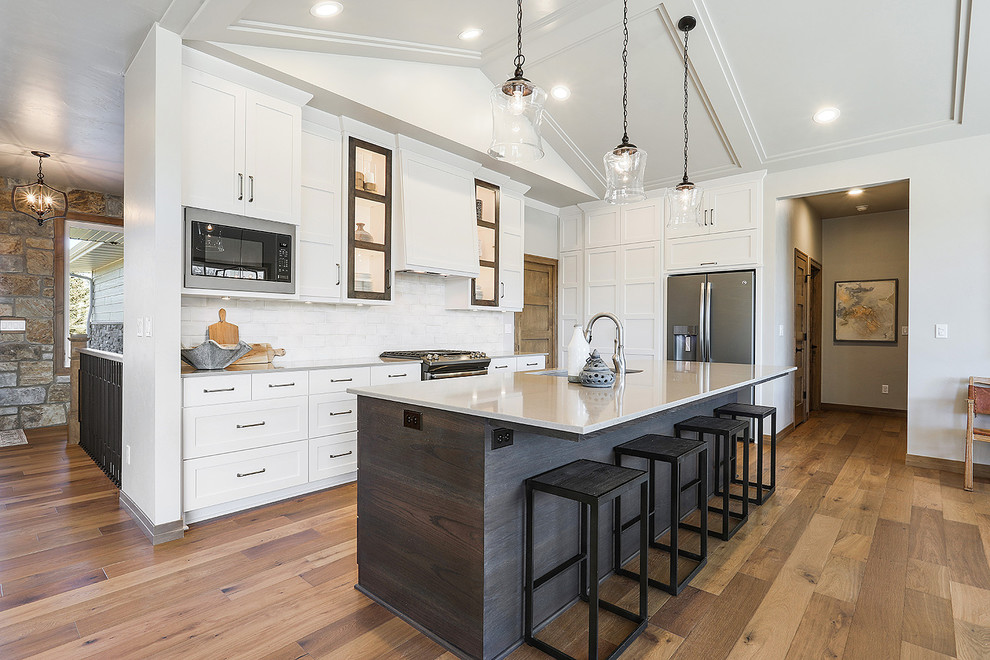 Inspiration for a mid-sized transitional l-shaped kitchen in Other with an undermount sink, white cabinets, quartz benchtops, white splashback, ceramic splashback, stainless steel appliances, medium hardwood floors, with island, brown floor, shaker cabinets and white benchtop.