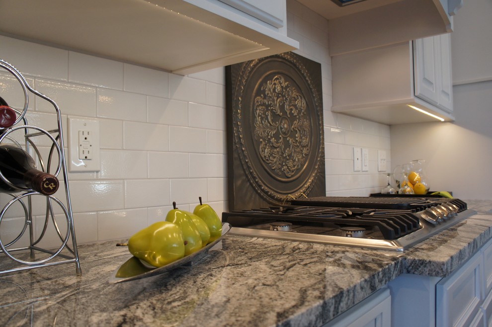Example of a transitional single-wall dark wood floor open concept kitchen design with a farmhouse sink, raised-panel cabinets, white cabinets, granite countertops, white backsplash, stainless steel appliances and an island