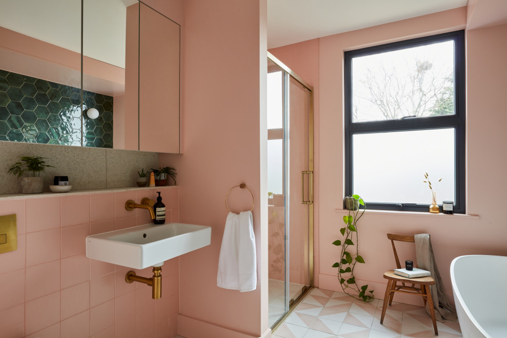 Mid-sized contemporary kids bathroom in London with a freestanding tub, a curbless shower, a wall-mount toilet, pink tile, ceramic tile, pink walls, cement tiles, a wall-mount sink, terrazzo benchtops, pink floor, a sliding shower screen, multi-coloured benchtops, a single vanity and a built-in vanity.