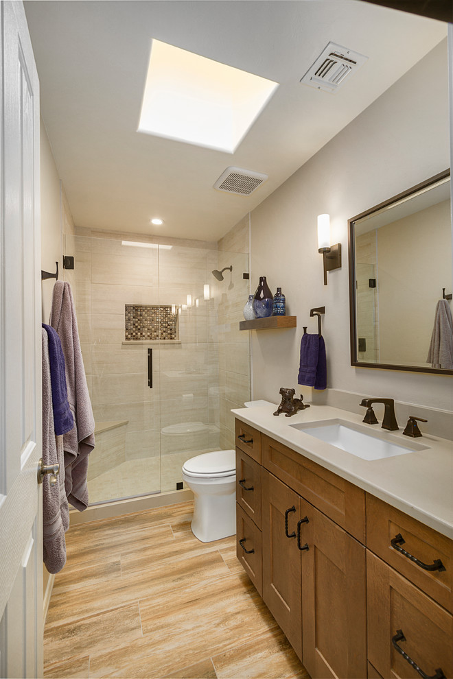 This is an example of a small country 3/4 bathroom in Phoenix with shaker cabinets, medium wood cabinets, an alcove shower, a one-piece toilet, beige tile, porcelain tile, beige walls, porcelain floors, an undermount sink, engineered quartz benchtops, brown floor, a hinged shower door and beige benchtops.