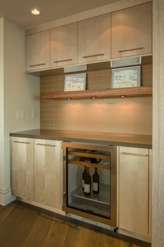 This is an example of a mid-sized contemporary single-wall home bar in San Francisco with no sink, flat-panel cabinets, light wood cabinets, dark hardwood floors and beige splashback.