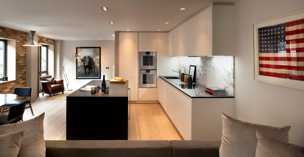 Photo of a mid-sized contemporary l-shaped eat-in kitchen in London with an integrated sink, stone slab splashback, light hardwood floors, with island and stainless steel appliances.