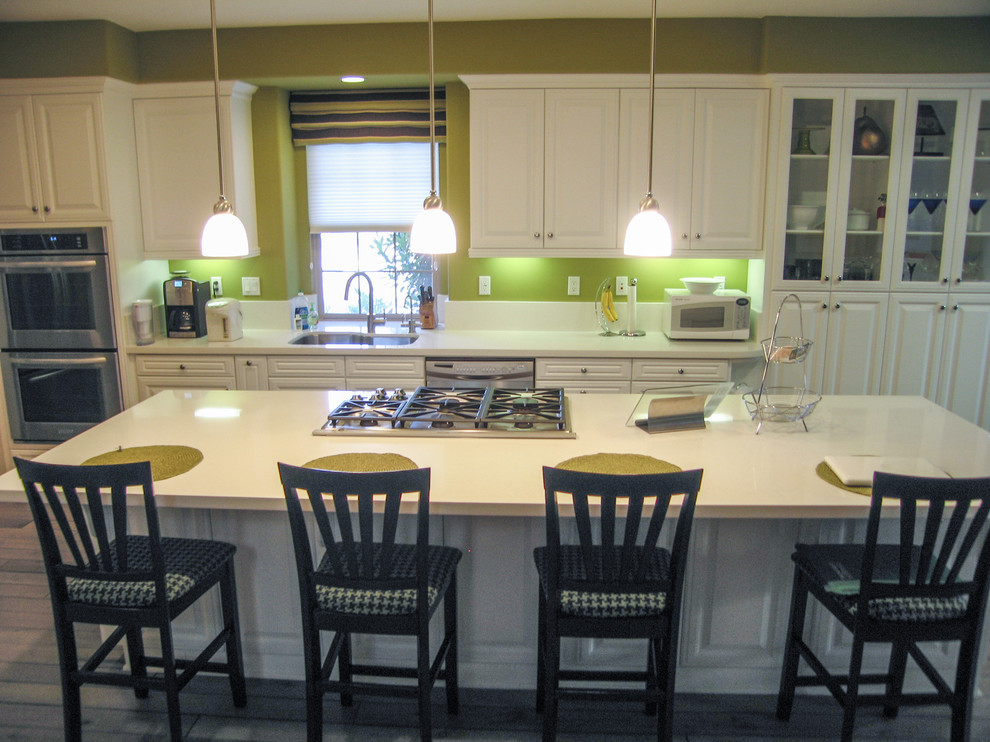 Example of a mid-sized trendy galley light wood floor open concept kitchen design in Orange County with an undermount sink, raised-panel cabinets, white cabinets, quartzite countertops, green backsplash, stone slab backsplash, stainless steel appliances and an island