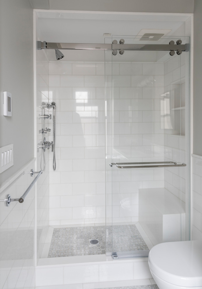 Klassisk inredning av ett mellanstort vit vitt badrum, med grå skåp, en dusch i en alkov, en vägghängd toalettstol, vit kakel, marmorkakel, vita väggar, marmorgolv, ett undermonterad handfat, bänkskiva i glas, grått golv och dusch med skjutdörr