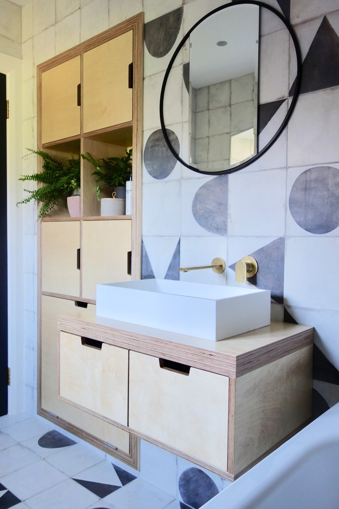 This is an example of a scandinavian kids bathroom in Other with light wood cabinets, a drop-in tub, a shower/bathtub combo, a one-piece toilet, black and white tile, porcelain tile, white walls, porcelain floors, a console sink, wood benchtops and multi-coloured floor.
