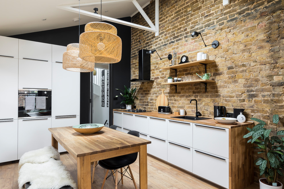 Inspiration for an industrial kitchen in London with a drop-in sink, flat-panel cabinets, white cabinets, wood benchtops, stainless steel appliances, medium hardwood floors, with island and brown floor.