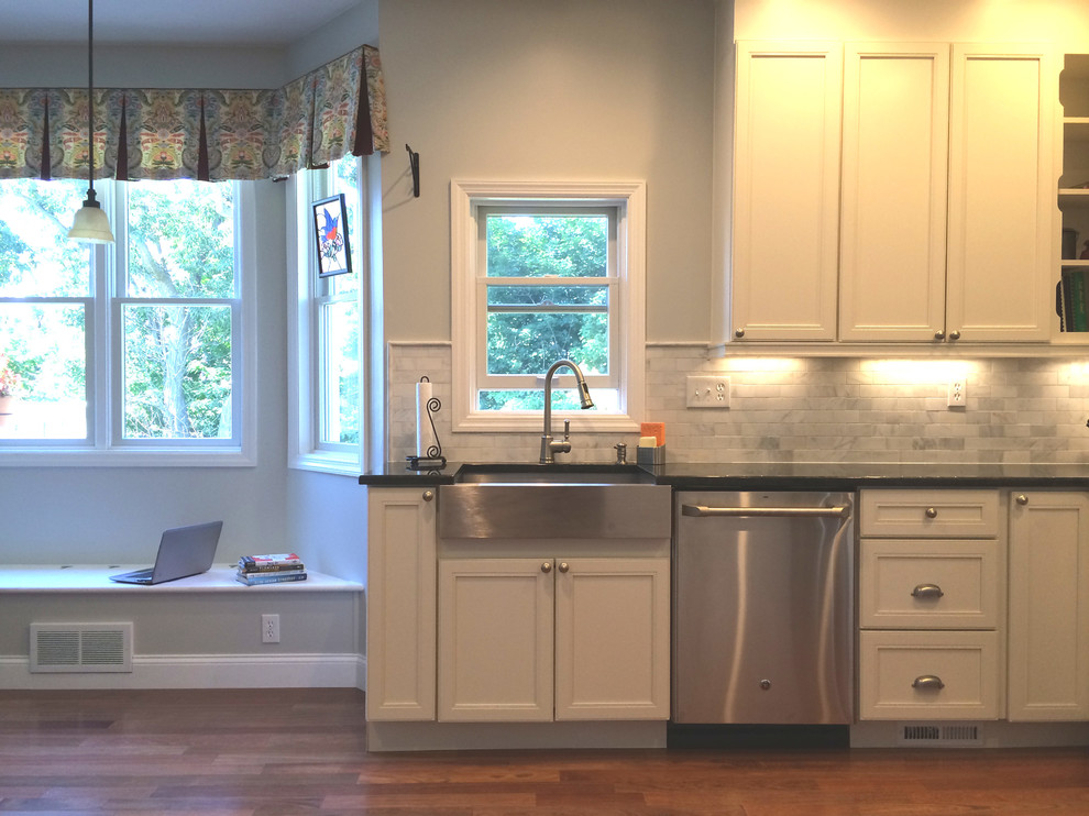 Inspiration for a transitional u-shaped medium tone wood floor eat-in kitchen remodel with a farmhouse sink, raised-panel cabinets, white cabinets, granite countertops, multicolored backsplash, stone tile backsplash, stainless steel appliances and no island
