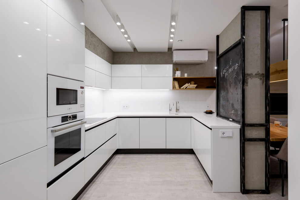 Photo of a contemporary u-shaped kitchen in Moscow with an integrated sink, flat-panel cabinets, white cabinets, white splashback, white appliances, grey floor and white benchtop.