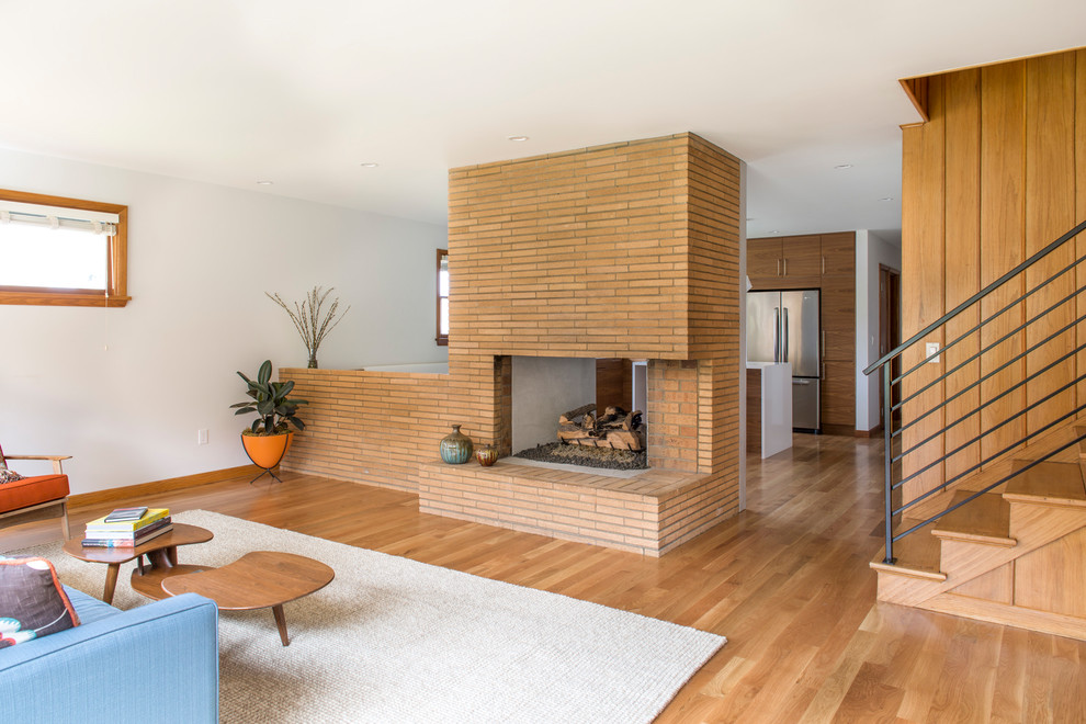 Mid-sized midcentury open concept living room in Portland with white walls, medium hardwood floors, a two-sided fireplace, a brick fireplace surround and a concealed tv.