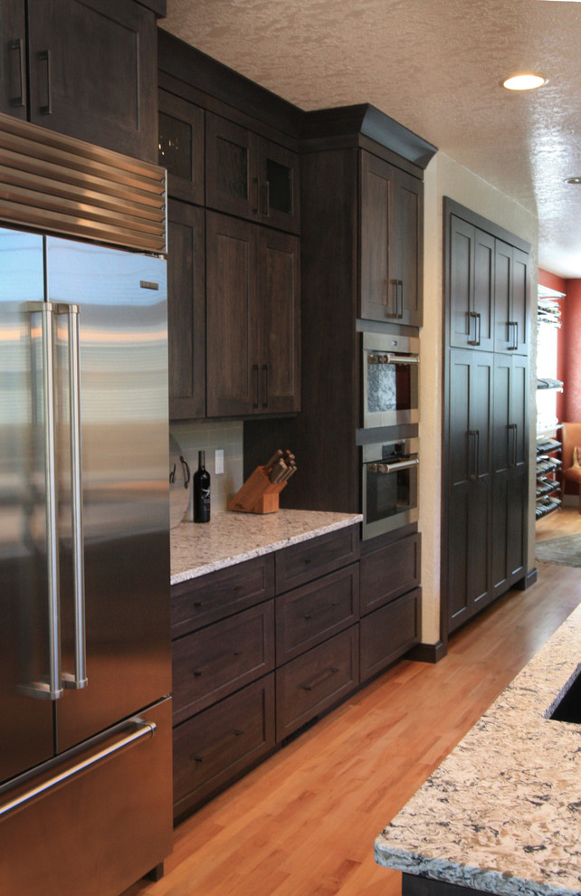 Inspiration for a large transitional u-shaped light wood floor eat-in kitchen remodel in Cedar Rapids with an undermount sink, shaker cabinets, dark wood cabinets, granite countertops, gray backsplash, glass tile backsplash, stainless steel appliances and an island