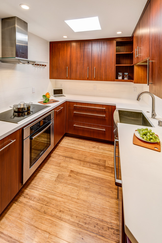 This is an example of a small contemporary u-shaped eat-in kitchen in San Francisco with a farmhouse sink, flat-panel cabinets, dark wood cabinets, solid surface benchtops, white splashback, porcelain splashback, stainless steel appliances, bamboo floors and no island.