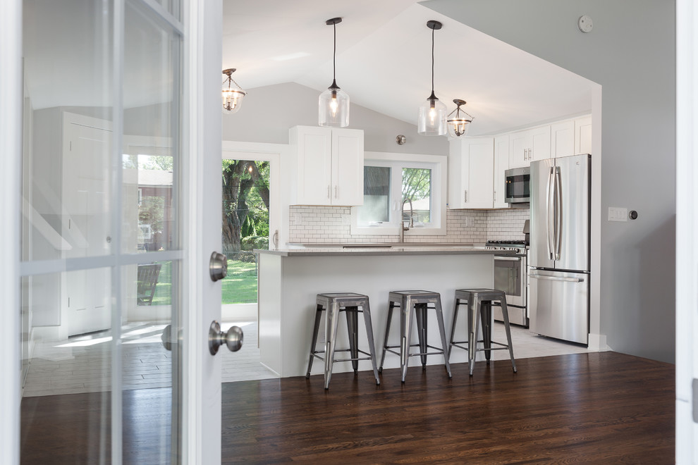 Inspiration for a large transitional l-shaped ceramic tile open concept kitchen remodel in Chicago with an undermount sink, shaker cabinets, white cabinets, quartz countertops, white backsplash, subway tile backsplash, stainless steel appliances and an island